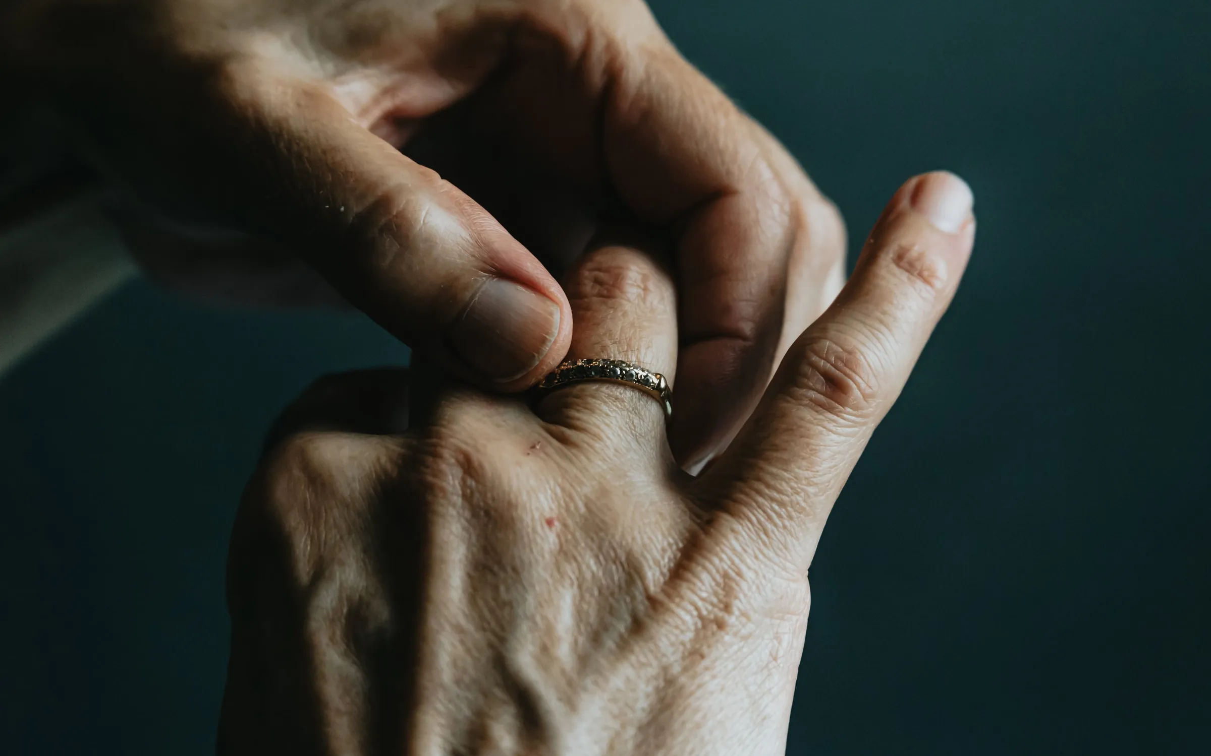 Two hands with a gold ring against a deep green background